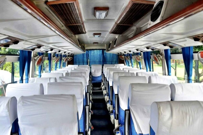 A train interior with rows of white-covered seats, blue curtains, and overhead fans. 3