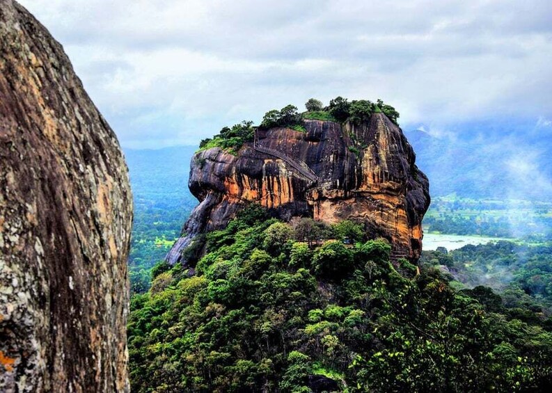 A large rock formation with a forested peak and a river in the background. 1
