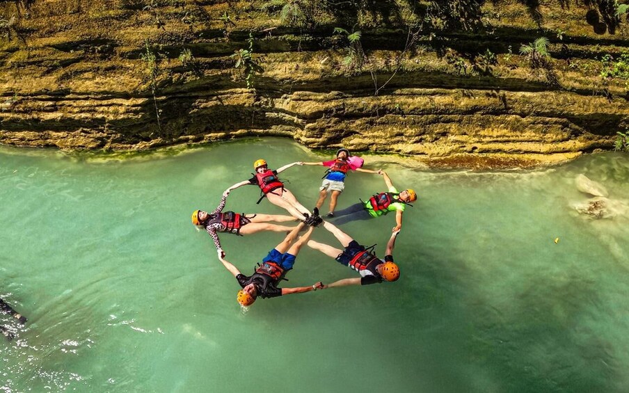 Four people skydiving in formation over a clear body of water with rocky cliffs in the background. 1