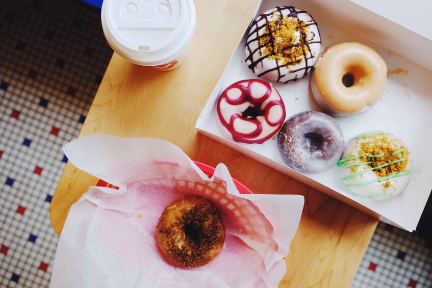 A box of assorted donuts with various toppings and a coffee cup. 1