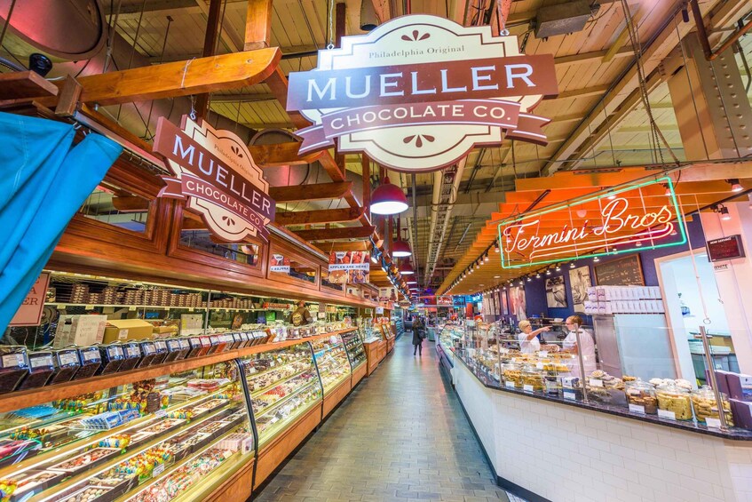 An indoor market with wooden beams and hanging signs for chocolate shops like Mueller and Termini Bros. 2