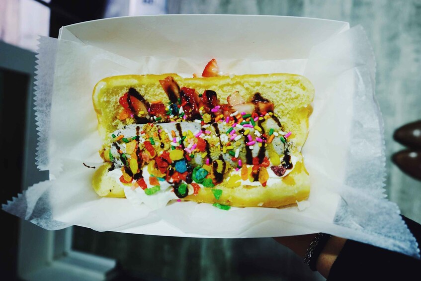 A pastry with colorful sprinkles and drizzled chocolate on a white paper. 3