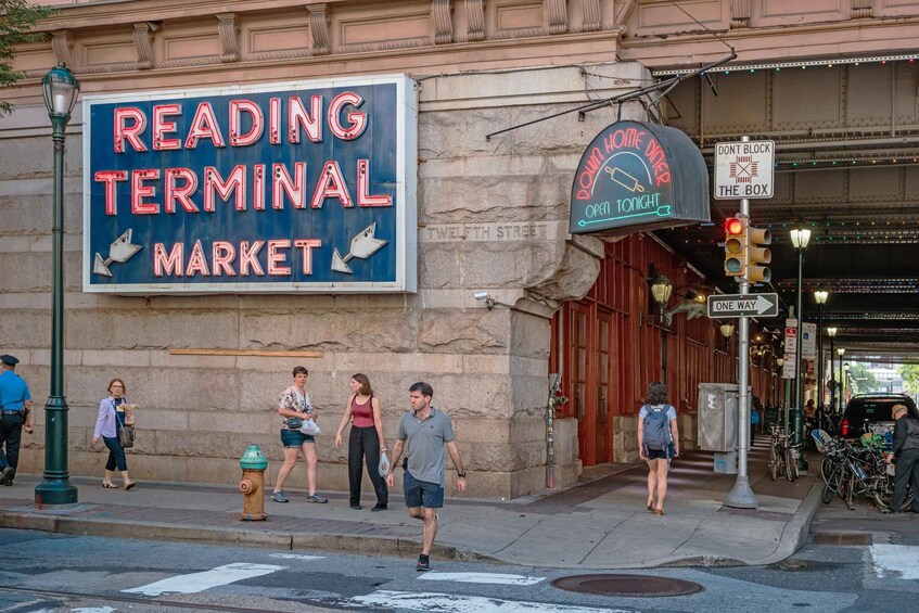 A street with a neon sign for Reading Terminal Market, a fire hydrant, and pedestrians. 4