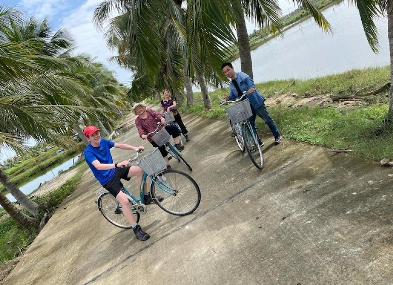 Four people riding bicycles on a concrete path surrounded by palm trees and a body of water. 5