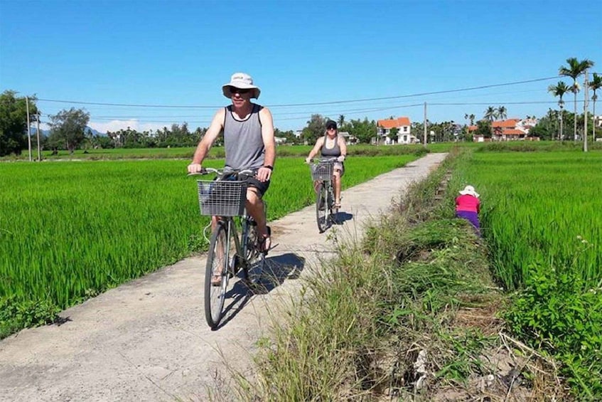 Two people riding bicycles on a rural path through a green field. 3