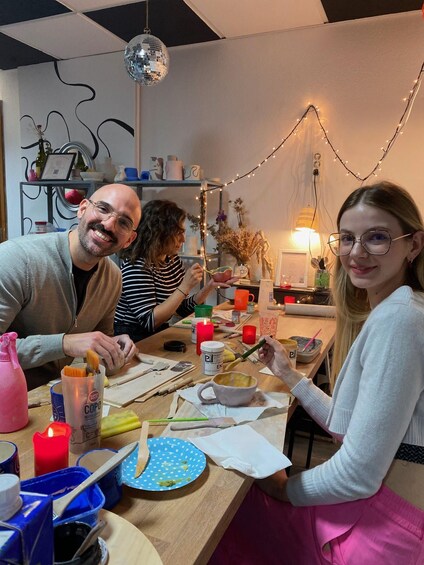 Three people sitting at a table with art supplies, engaged in a creative activity. 5