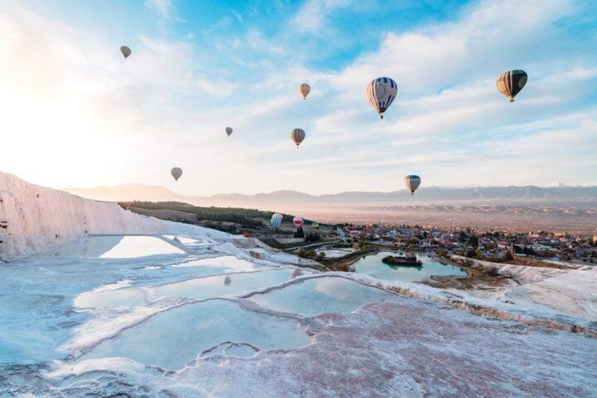 Varmluftsballonger svävar över ett landskap med saltformationer och en stad i bakgrunden. 1