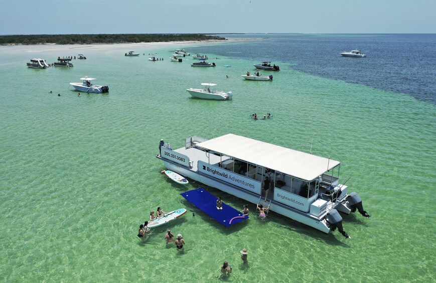 A boat named Brightwild Adventures on clear turquoise water with several smaller boats and people swimming and snorkeling nearby. 2