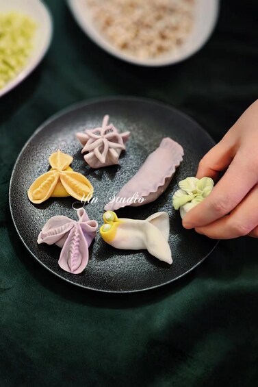 A black plate with various colorful food items, including a flower-shaped pastry and a rolled pastry, on a dark green cloth. 1