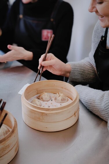 A person holding chopsticks over a bamboo steamer with dumplings. 4