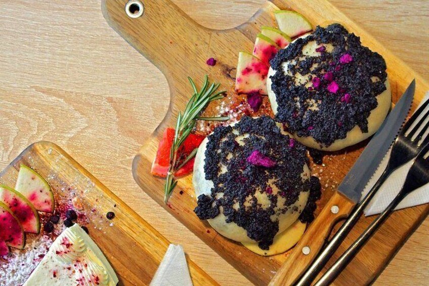 Twee ronde desserts op een houten plank, versierd met roze en paarse eetbare bloemen, met een mes en vork. 1