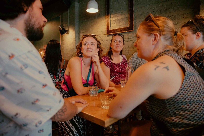 A group of people sitting around a wooden table in a cafe with brick walls and hanging lights. 4