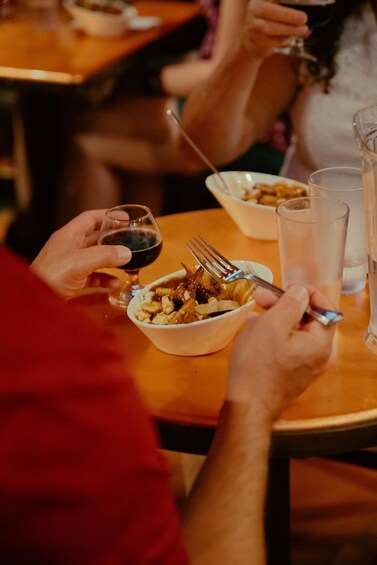 A person holding a wine glass and a fork over a bowl of food. 3