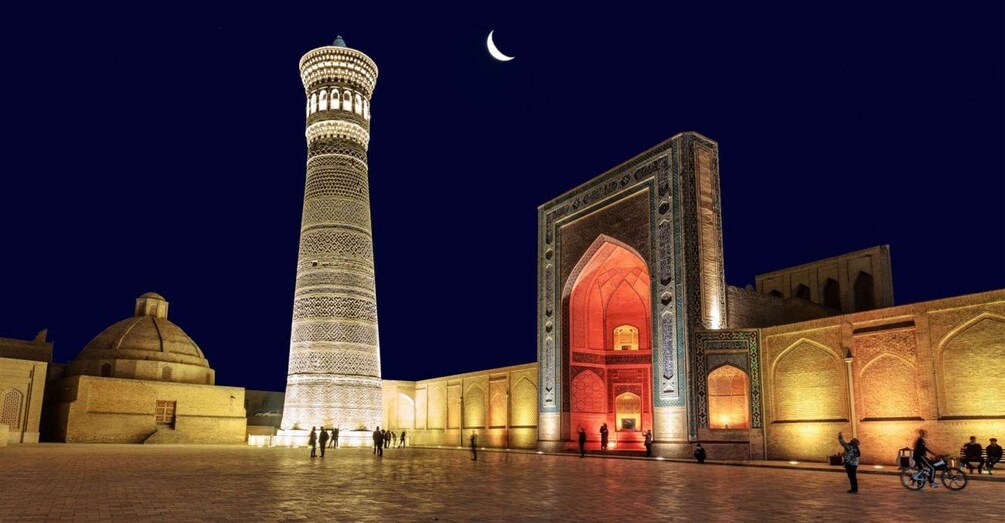 A mosque with a tall minaret and a large archway, illuminated at night. 3