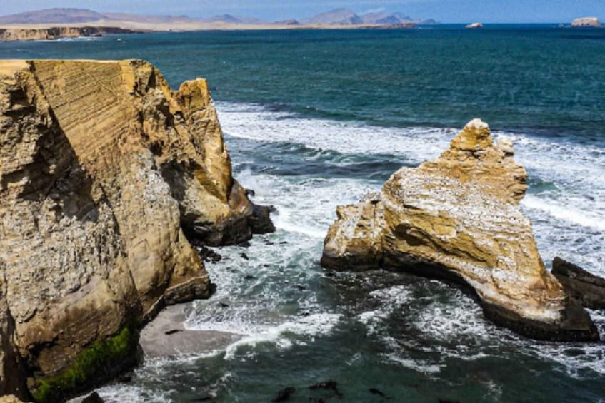 A coastal landscape with large rock formations and waves crashing against them. 2