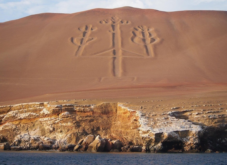 A desert landscape with a large sand dune and a rock formation with carved figures. 4