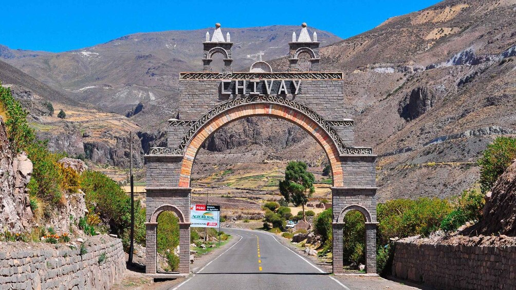 An archway with 'CHIVAY' and 'PERU' signage, a road leading through a mountainous landscape. 1