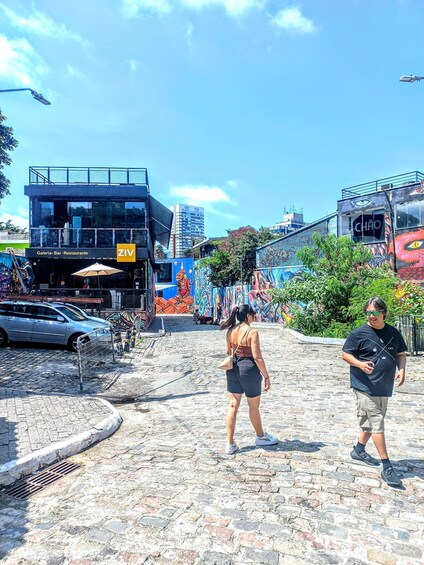 A street with cobblestones, a black building with a yellow sign, and colorful graffiti. 1