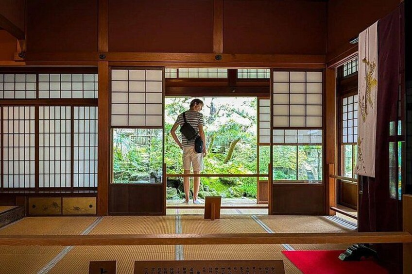 A traditional Japanese room with tatami flooring, sliding doors, and a view of greenery outside. 4