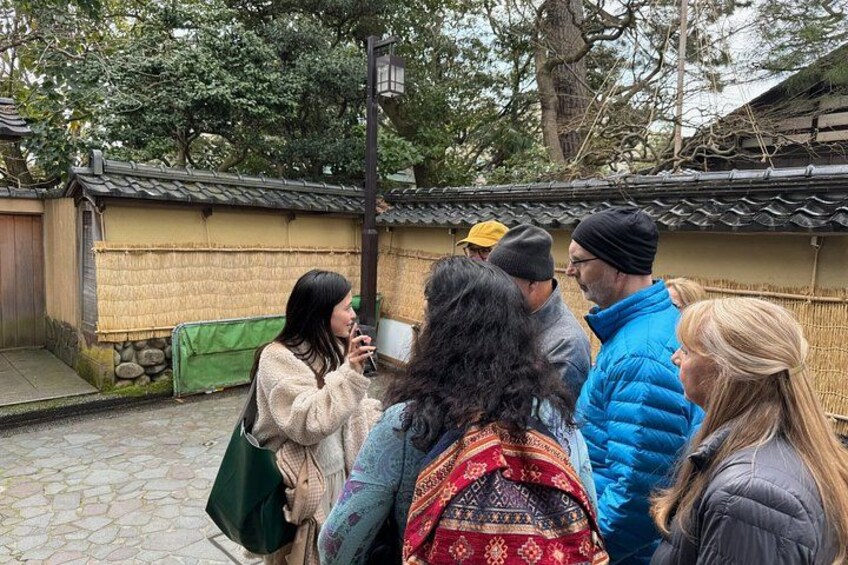 A group of people standing in a traditional Japanese courtyard with stone walls and a thatched roof. 3
