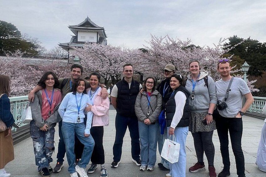 A group of people standing in front of a traditional building with cherry blossoms in the background. 3