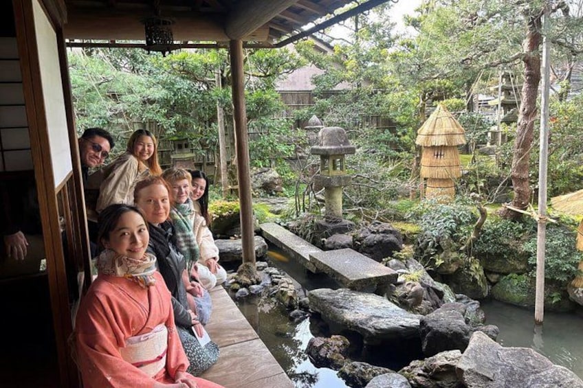 A group of people in traditional attire sitting by a stone bridge over a pond in a Japanese garden. 2