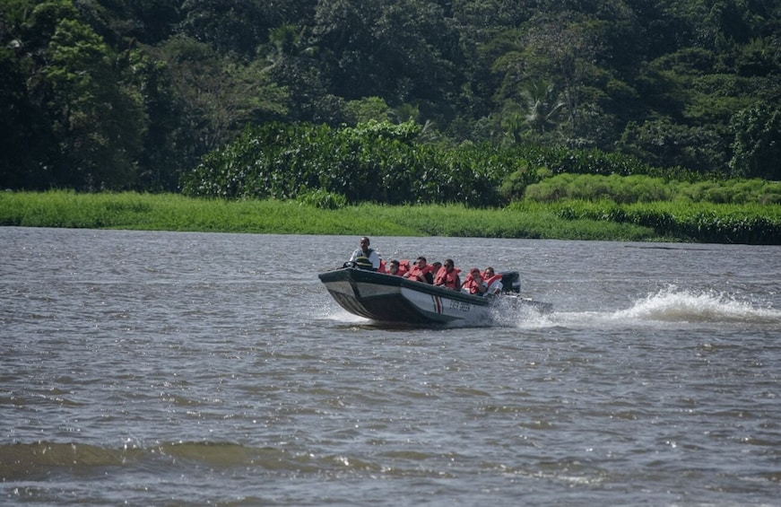A boat speeding across a river with passengers wearing life jackets. 1