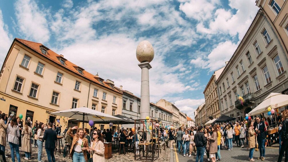 A crowded square with a central column topped by a sphere, surrounded by historic buildings. 4