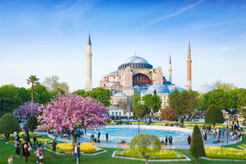 A large mosque with multiple domes and minarets, surrounded by a well-maintained garden with flowering trees and a central fountain. 1
