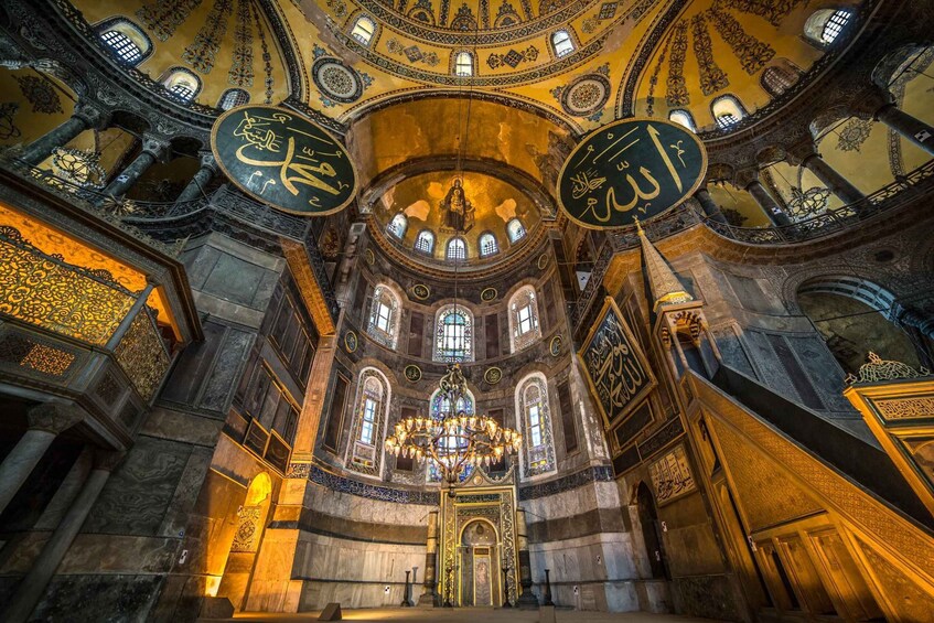 An ornate interior with a large chandelier, intricate ceiling designs, and Arabic calligraphy. 2