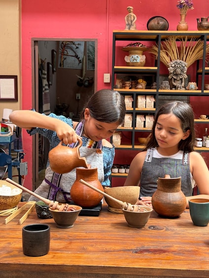 Two people engaged in pottery making, with various clay pots and tools on a wooden table. 1
