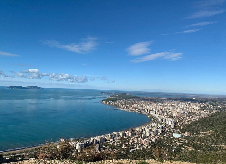 A coastal city with a clear blue sea, a curved coastline, and a hilly landscape. 1