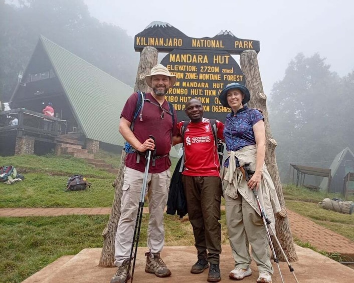 Three people standing in front of a sign at Kilimanjaro National Park. 5