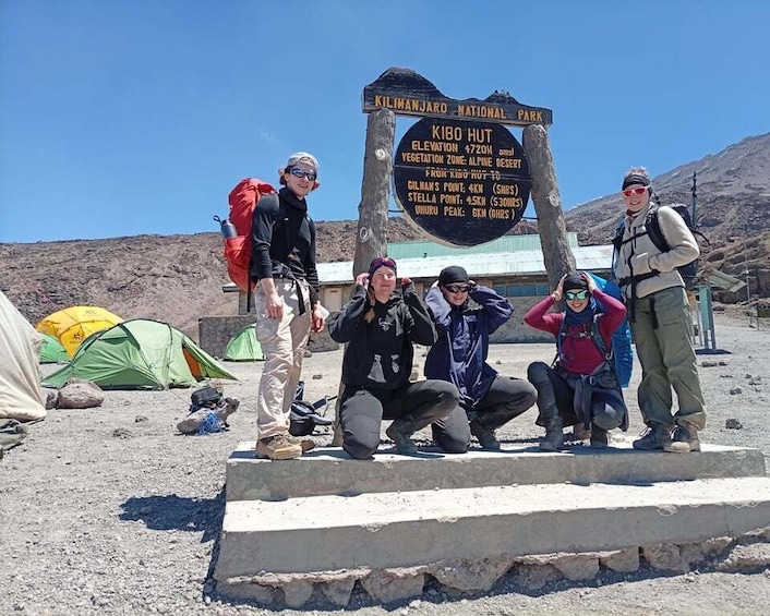 A group of hikers at Kibo Hut in Kilimanjaro National Park, with a sign indicating the elevation and distances to nearby points. 3