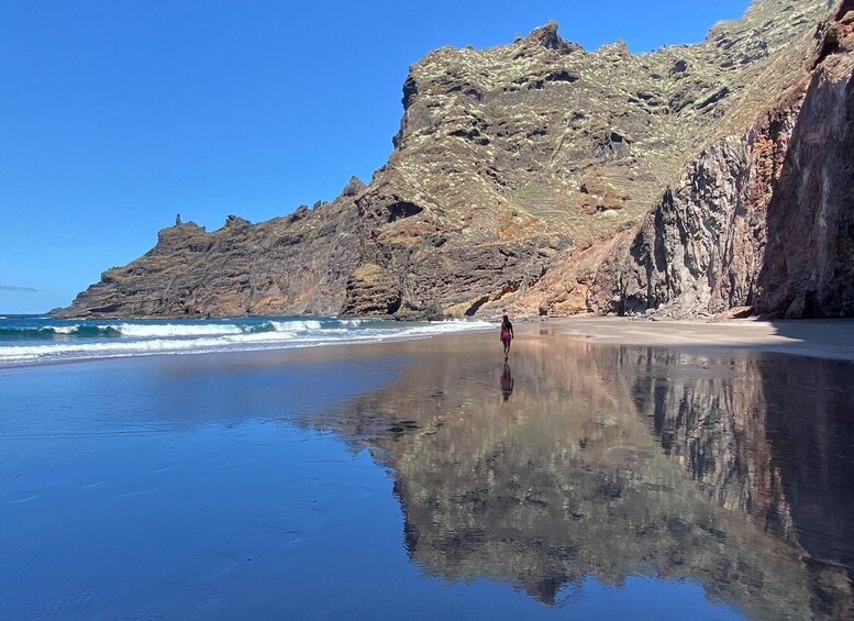 A beach with a rocky cliff and calm waters reflecting the scene. 1