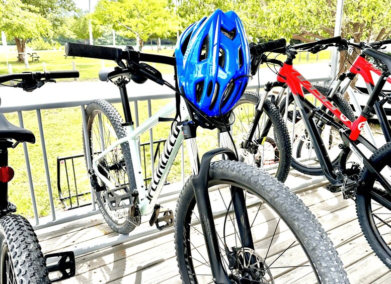 A white mountain bike with a blue helmet on the seat, a red bike, and a wooden deck. 4