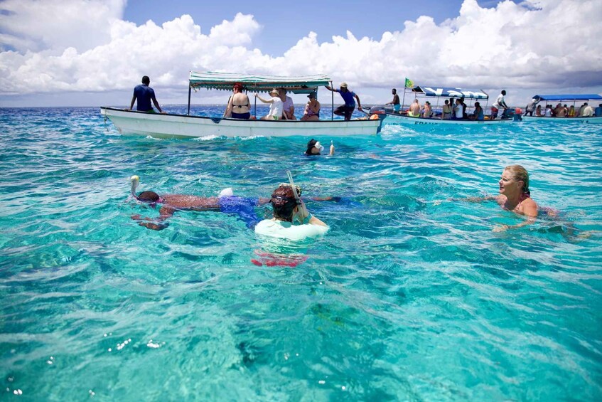 People swimming and floating on a clear blue sea, with boats in the background. 3