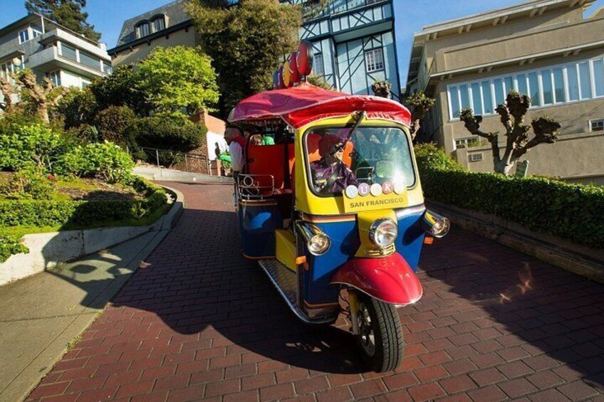 A colorful tuk-tuk parked on a brick path with greenery and buildings in the background. 4