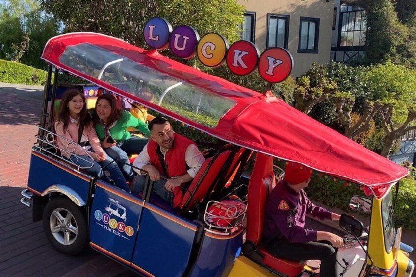 A colorful trolley with the word 'LUCKY' on the roof, passengers inside, and a building in the background. 5