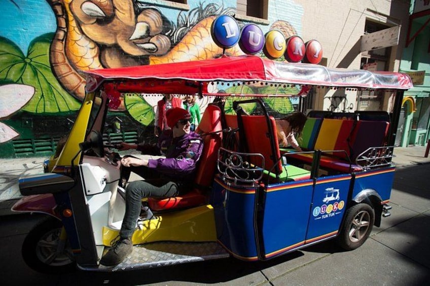 A colorful rickshaw parked on a street with a mural in the background. 3