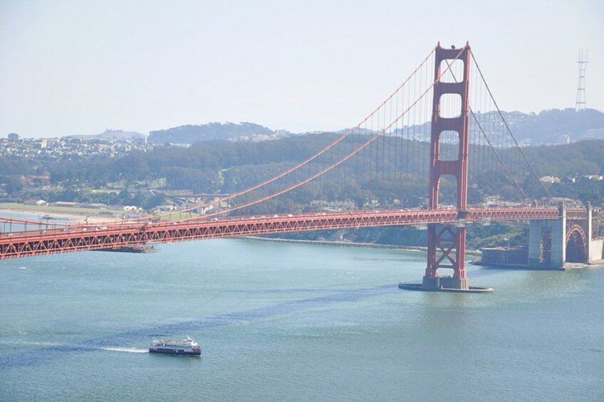 A large red suspension bridge spanning a body of water, with a boat in the foreground. 4