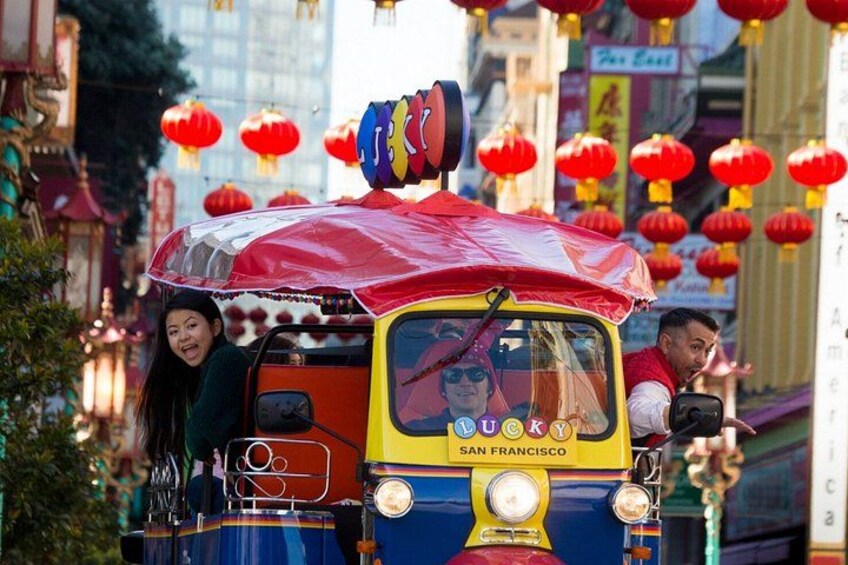 A colorful trolley with a red canopy, labeled 'Lucky San Francisco,' moving through a street decorated with red lanterns. 2
