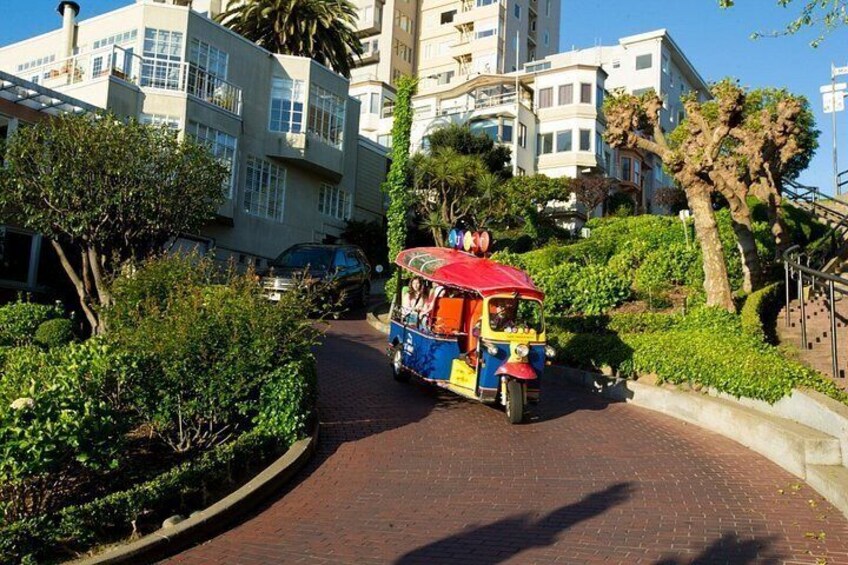 A colorful tuk-tuk on a paved path, surrounded by lush greenery and modern buildings. 3