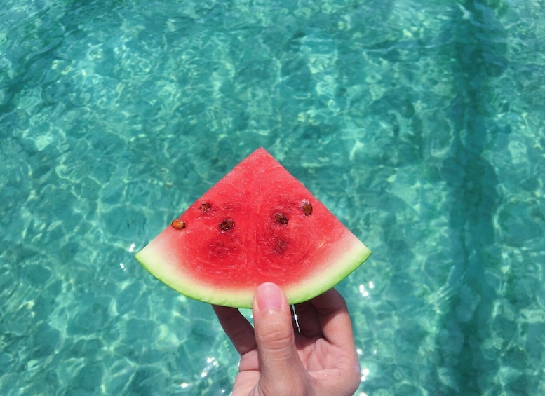 A slice of watermelon held above clear blue water. 2