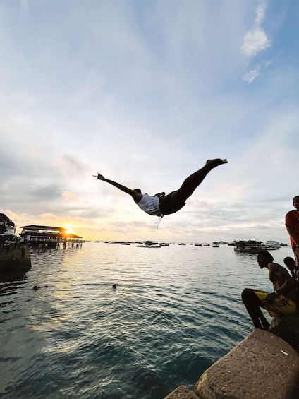 A person mid-air above water, with boats and a pier in the background. 5