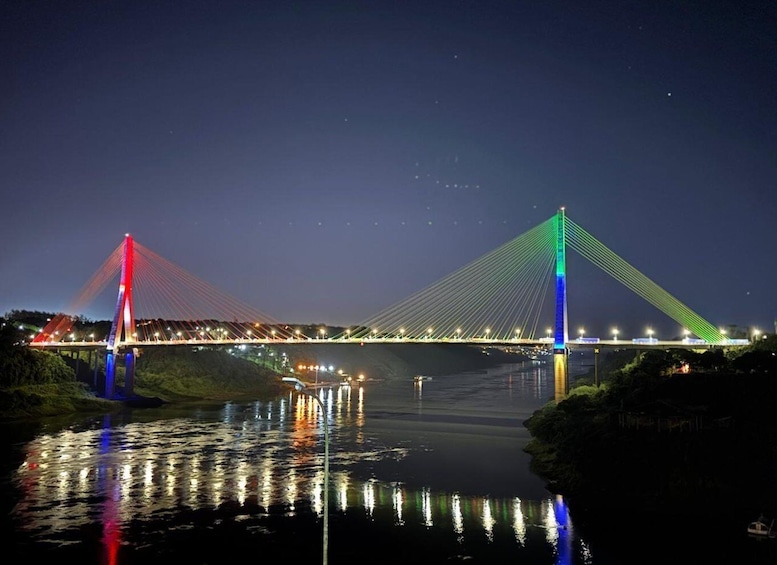 A brightly lit bridge at night with colorful lights reflecting on the water. 1