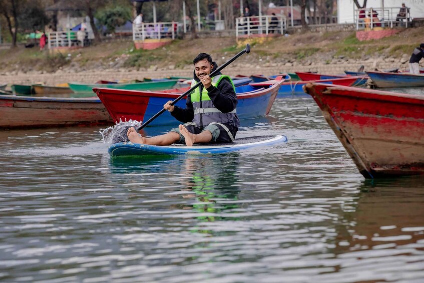 A person paddling a blue paddleboard in calm water with several boats in the background. 3