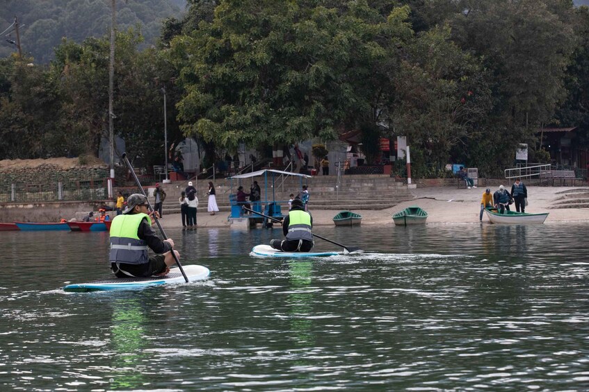People paddling on a calm river, surrounded by trees and a stone wall. 1