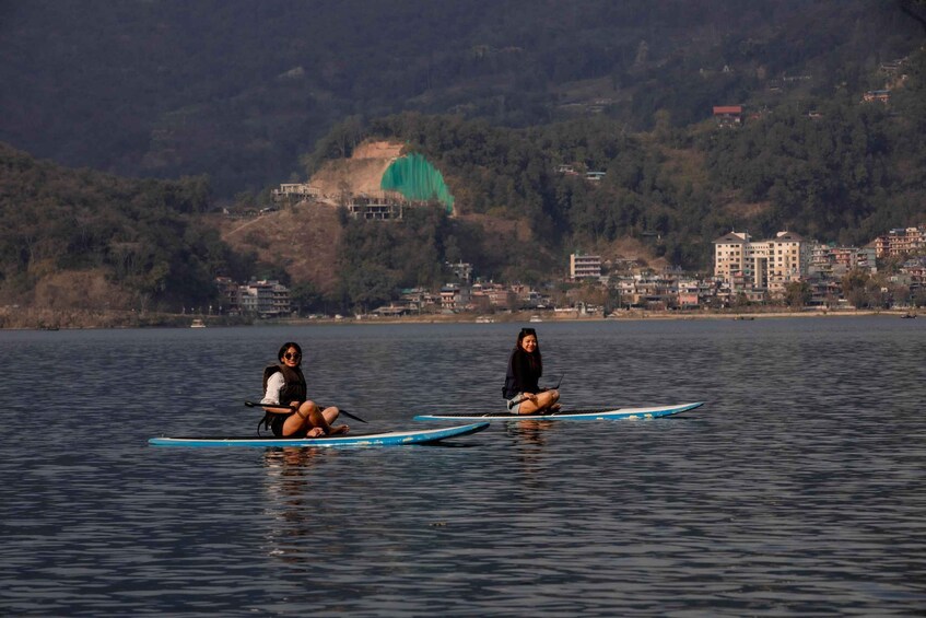 Two people on paddleboards in a calm body of water with a hilly landscape in the background. 5