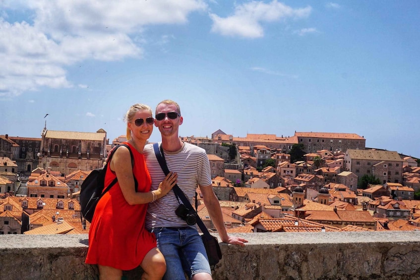 A couple sitting on a stone wall overlooking a historic town with red-roofed buildings. 2